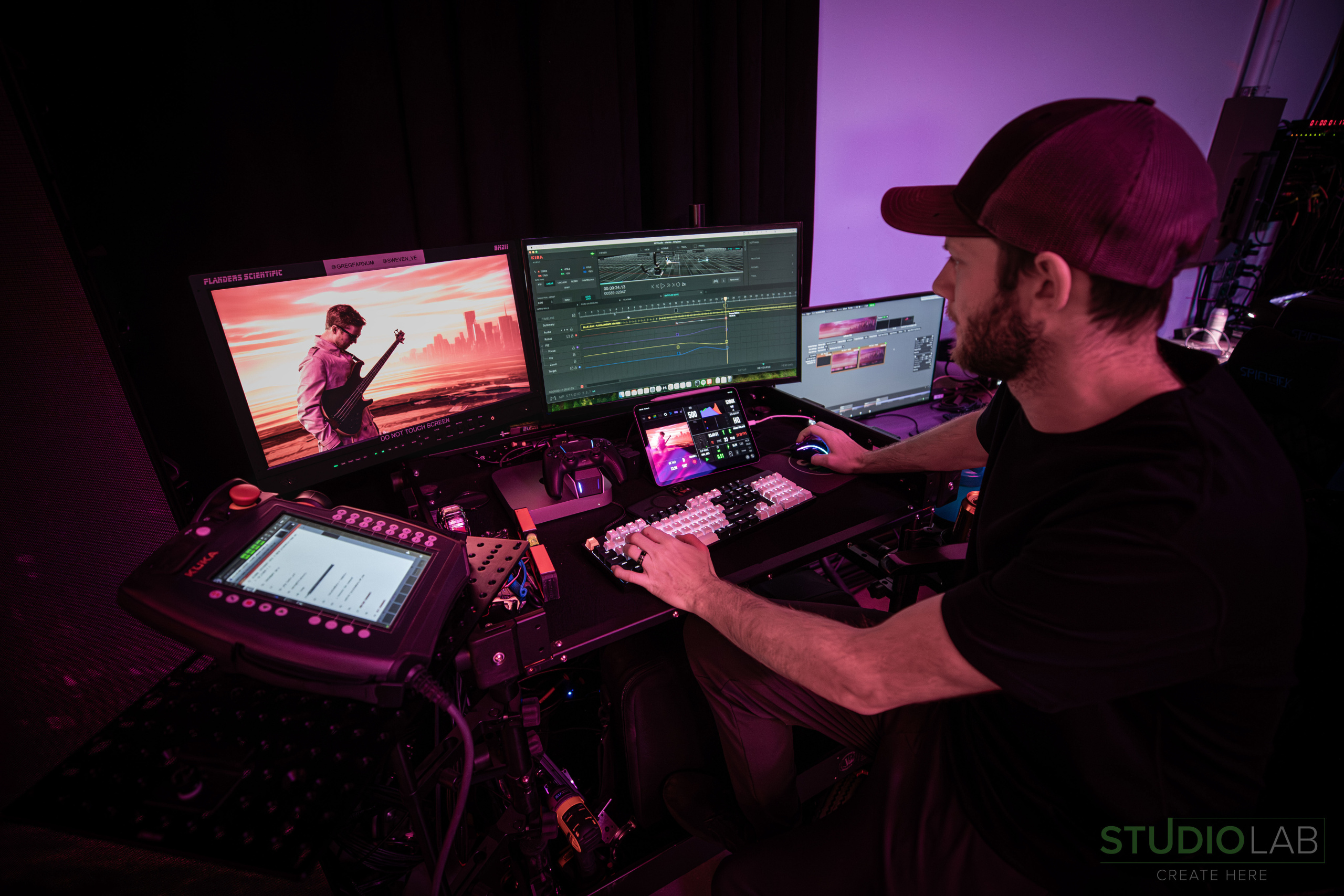 Person at a desk working on a multi-screen editing setup, with a music video scene displayed on the monitors in a dimly lit room.