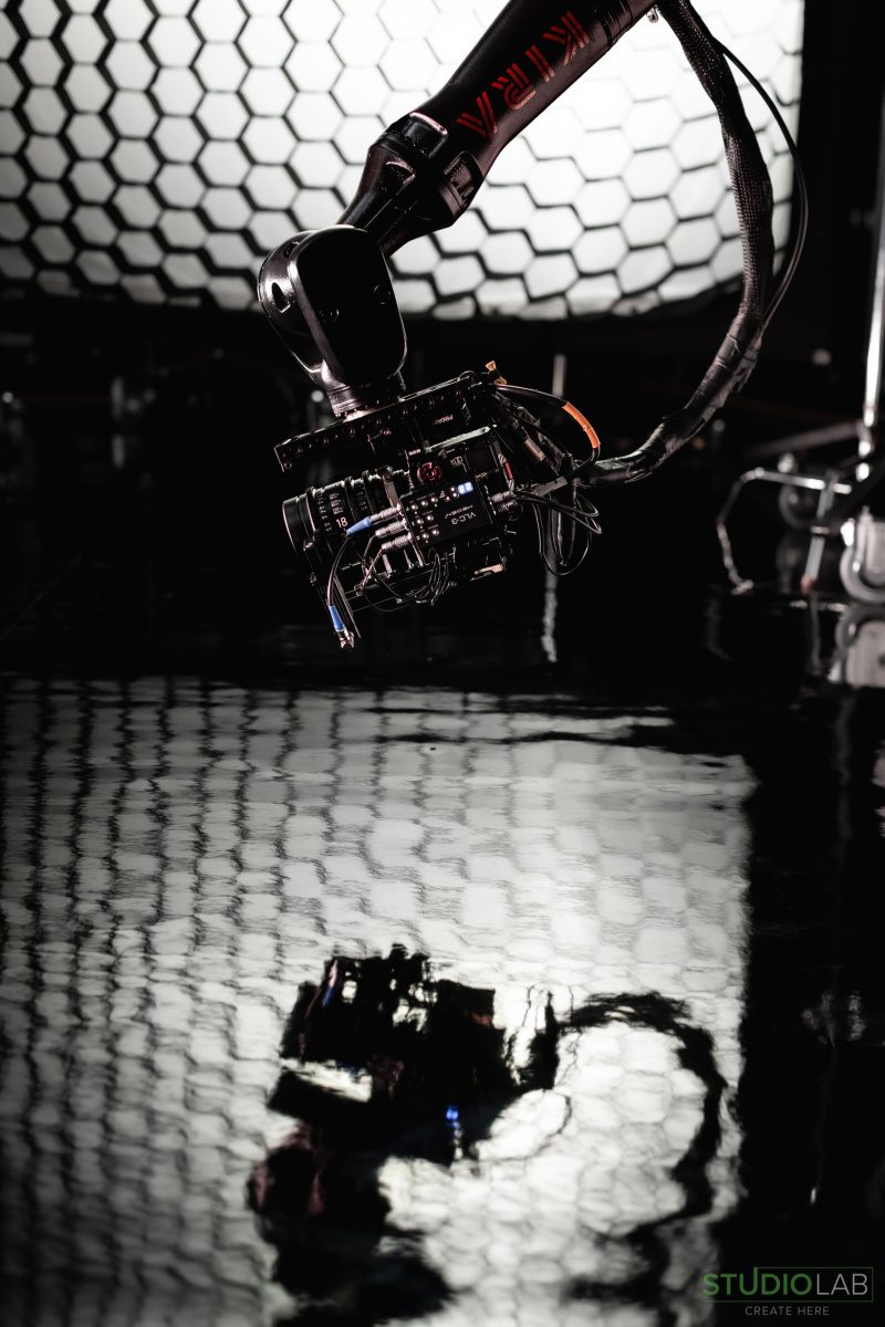 A close-up of a KIRA robotic camera arm, with its reflection in the glossy surface below, capturing footage on set.