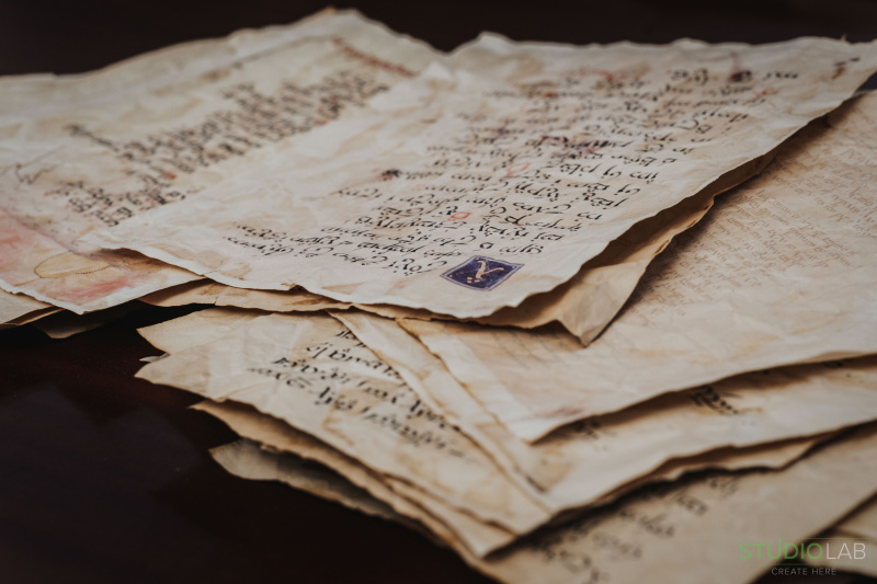 A stack of aged, handwritten letters with intricate script and a small, detailed stamp, resting on a dark wooden surface.