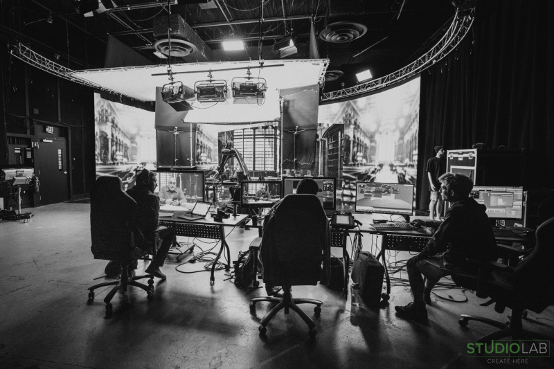 A wide shot of a studio control room, where technicians are working at desks filled with monitors, with a set visible in the background.