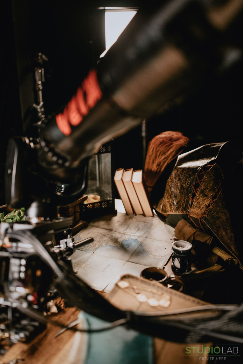 Close-up of the KIRA robotic arm maneuvering over an intricate table filled with old books, a map, and various ancient-looking props.