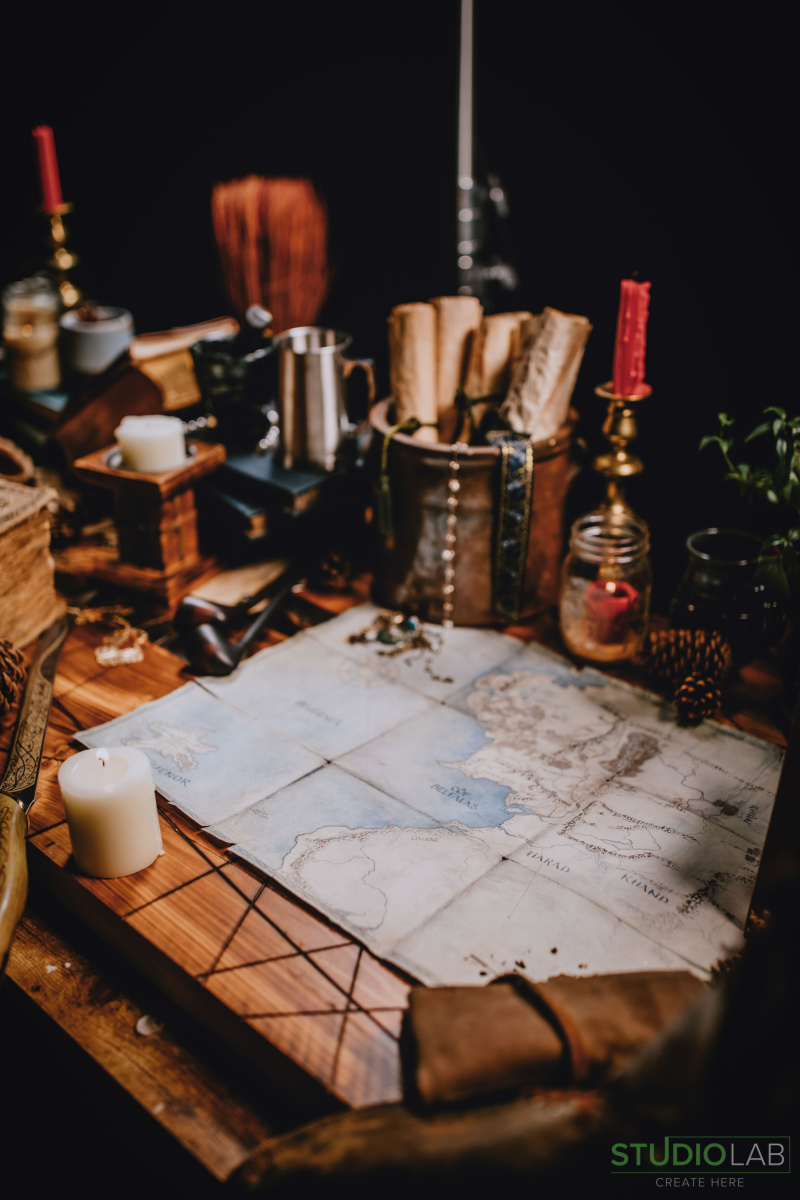 A table filled with medieval props like a candle, scrolls, a map, and books, creating a rustic and mysterious atmosphere.