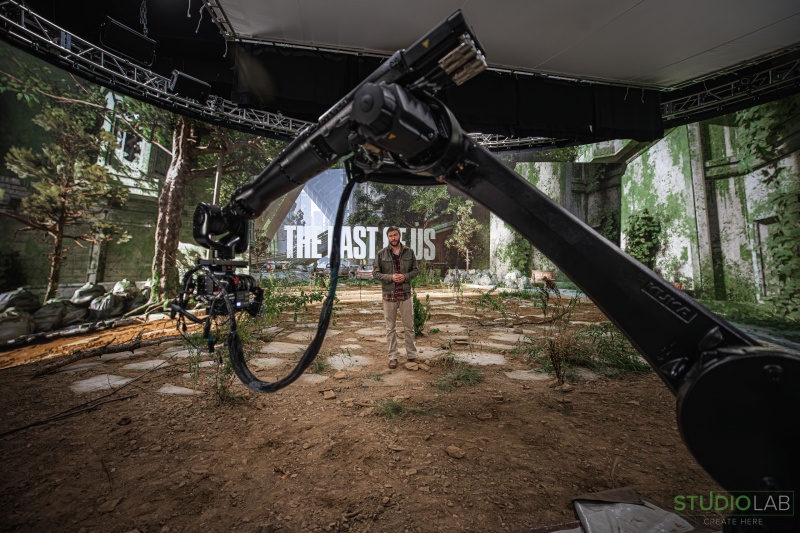 A man stands on a post-apocalyptic set. A robotic camera arm captures the scene, with "The Last of Us" displayed prominently.