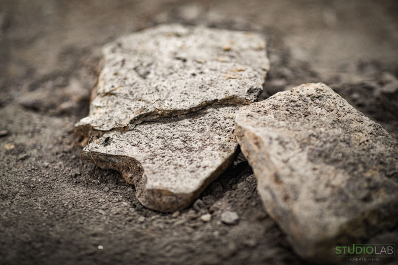 Close-up of broken concrete slabs resting on a dirt surface, capturing the rugged texture and weathered appearance of the post-apocalyptic environment.