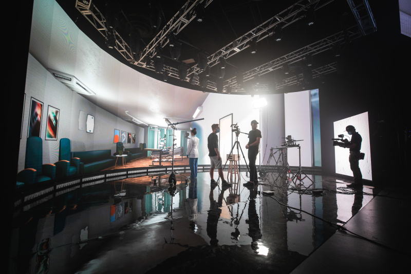 A film crew works on a realistic hospital set, with cameras and lighting equipment capturing the scene. The set includes hospital beds and medical decor.