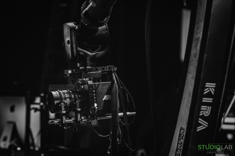 A close-up shot of a camera mounted on a robotic arm labeled "KIRA" captures the precision and technology used on set, highlighting the ARRI camera attached.