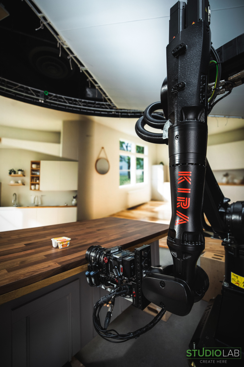A robotic camera arm is focused on a container of Hood Medleys cottage cheese sitting on a wooden table in a kitchen set, preparing for a shoot.